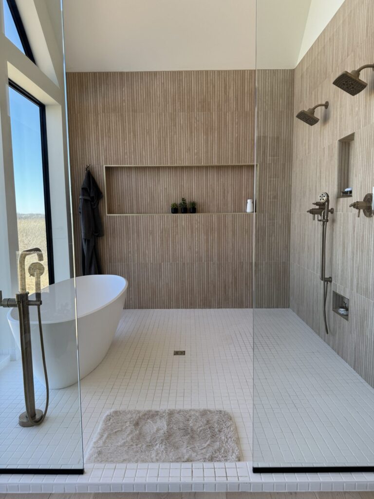 Wet room with slat wood style tile on the wall and cream color tile on the floor, white standing tub and niche shelf along the far wall