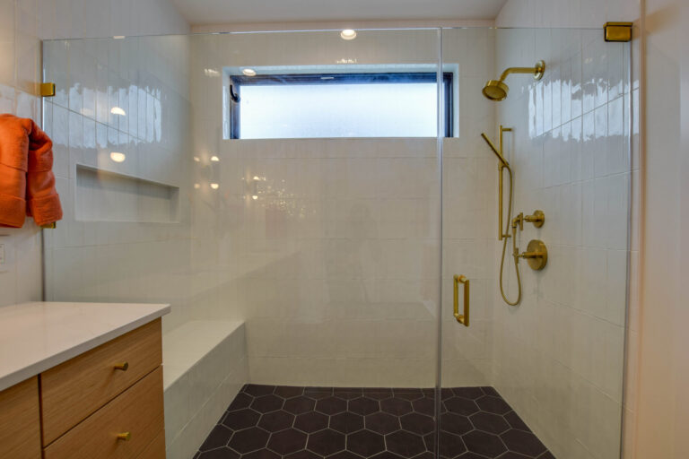 curbless walk in shower with white tile walls and black tile floors and a window on a long wall