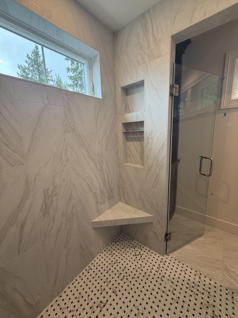 wet room with marble tile walls niche and corner bench and narrow window near ceiling