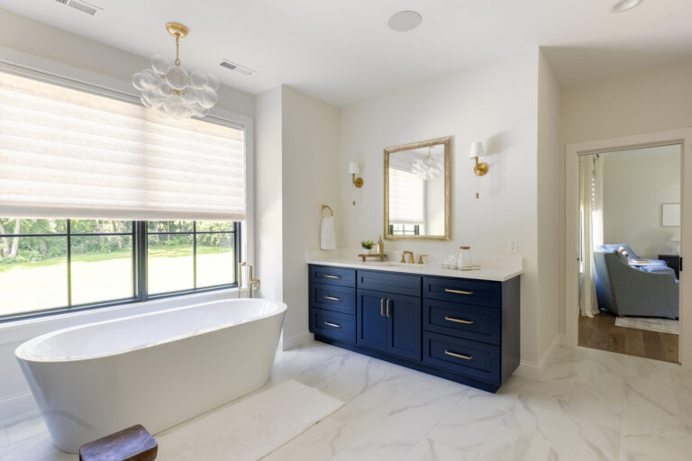 primary bathroom with marble floor free standing tub and blue and gold vanity with mirror
