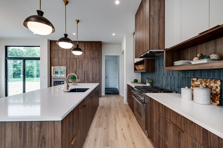 view of kitchen pathway between island that's wood and white countertop and white and wood cabinets with blue green tile backsplash