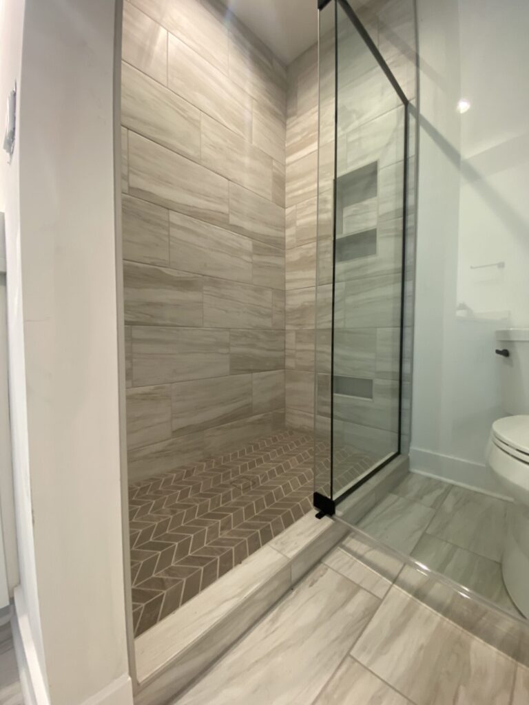 walk in shower with chevron pattern brown tile floor and beige marble pattern tile walls