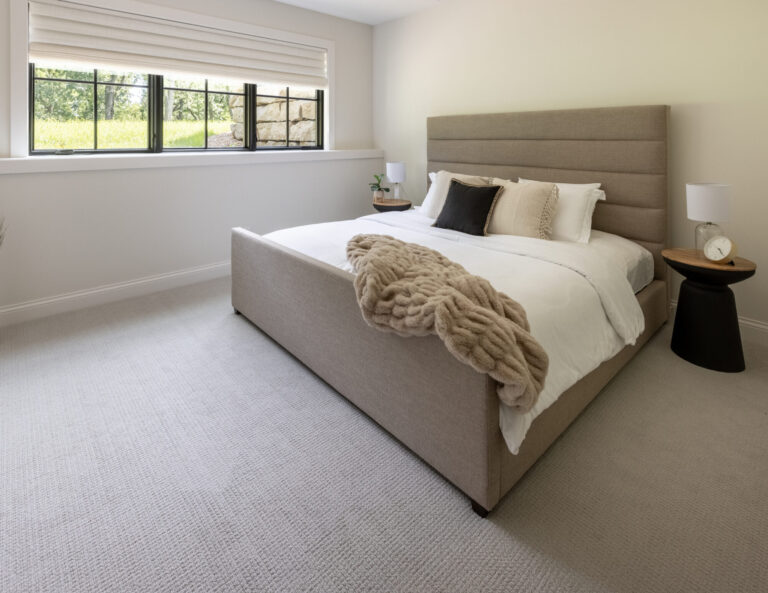 lower level bedroom with grey wall to wall carpeting and a queen size bed with upholstered headboard