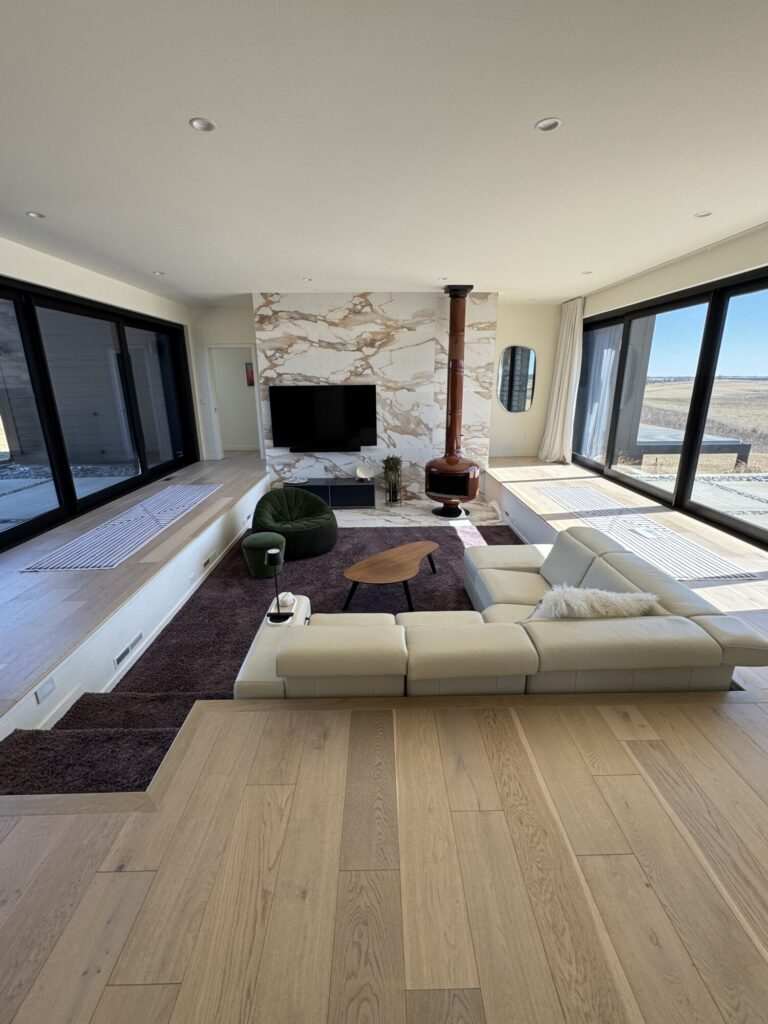 View of conversation pit style living room with purple shag carpet, cream leather sectional sofa, marble wall tile, tv on the wall tile and pot belly fireplace