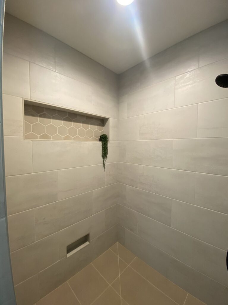 walk in shower with large stone beige tiles and shelf niche with beige hexagon tile accent