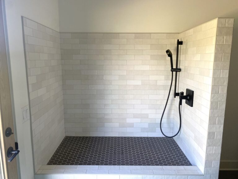 dog shower with white textured subway tile wall and small black hexagon tile floor black shower fixtures