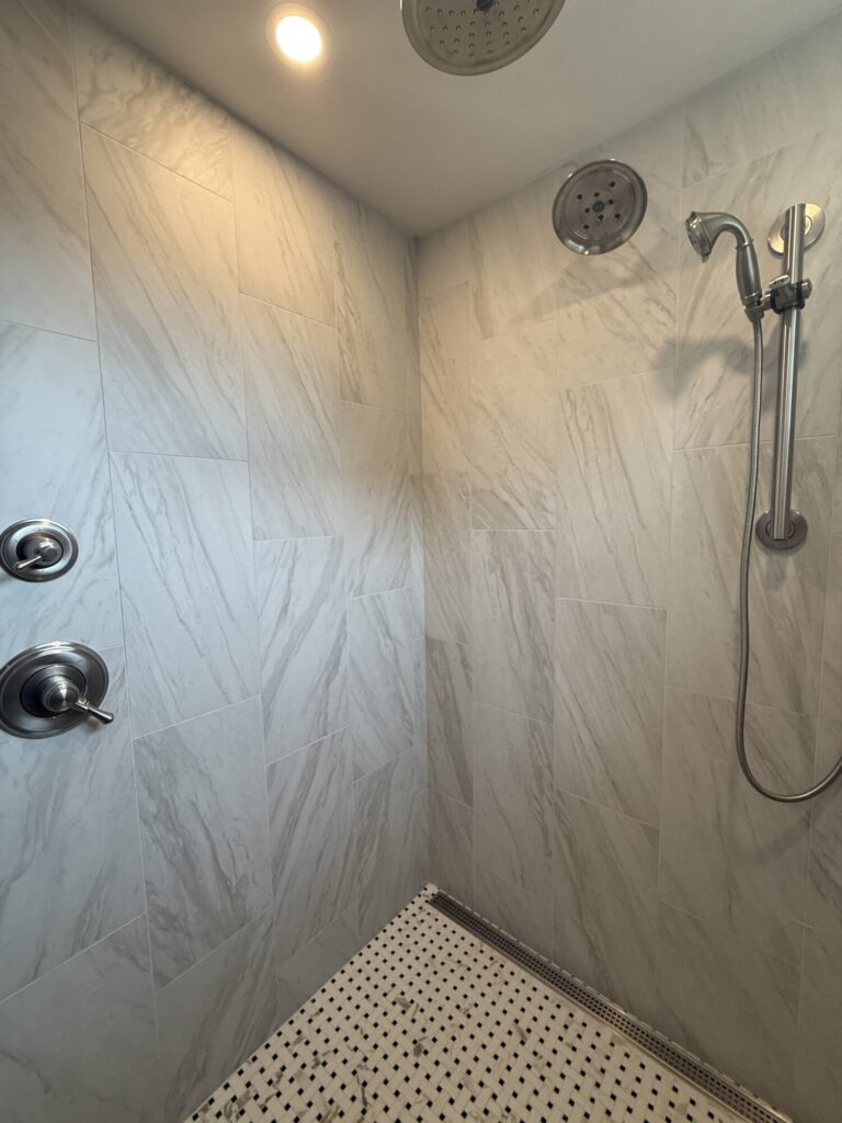shower room with silver shower head white marble tile walls and stone floor with black small geometric pattern