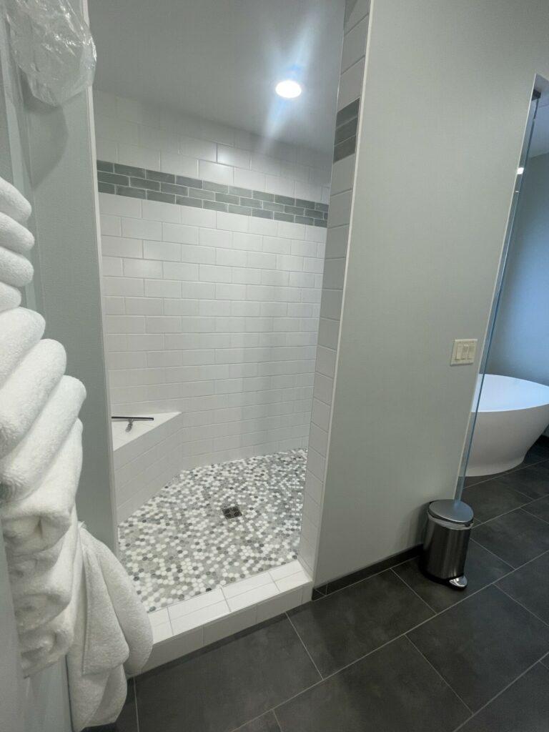 alcove shower with white tile walls and pebble tile floor