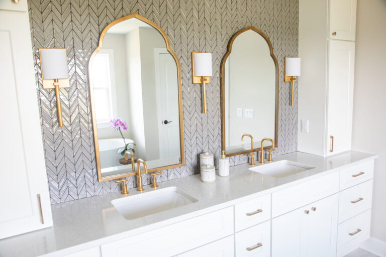chevron pattern grey wall tile behind two brass frame mirrors