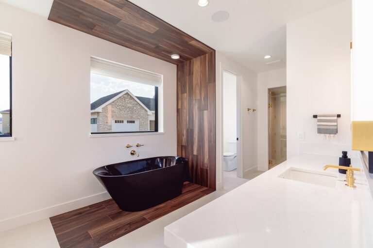 white bathroom with wood look tile detail surrounding a black free standing tub