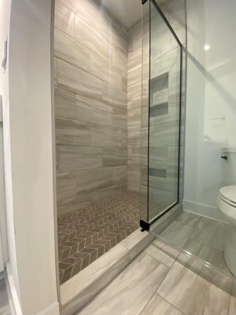 walk in shower with chevron pattern brown tile floor and beige marble pattern tile walls