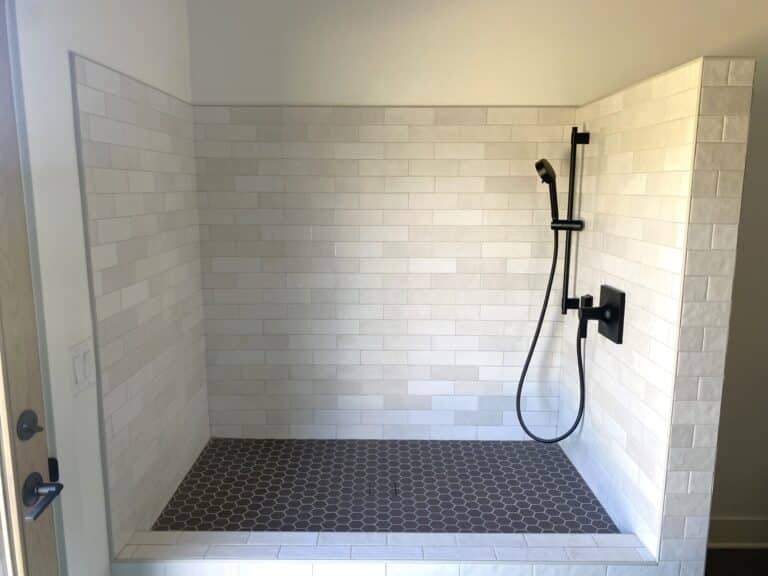 dog shower with white textured subway tile wall and small black hexagon tile floor black shower fixtures