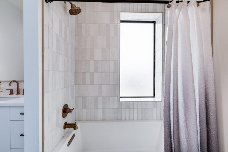 white tub and grey zellige tile on the wall and window on the long wall