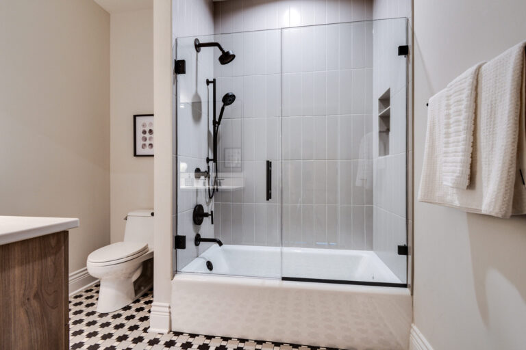 Tub and shower with white tub and grey tile to the ceiling with black plumbing fixtures