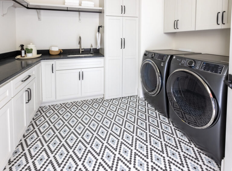 black and white mosaic geometric design tile floor in laundry room with white cabinets and black appliances