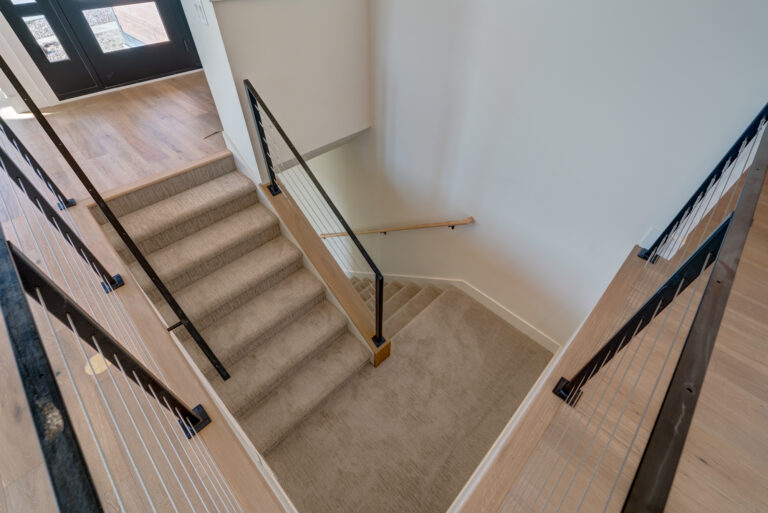 tan carpeting in hardwood stairs with black railing