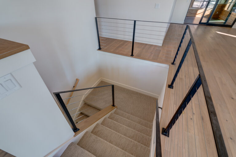 tan carpet stair runner with black railing and hardwood floor