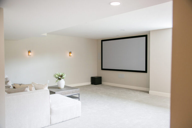 lower level tv area wall to wall grey carpeting white couch and large screen on the wall