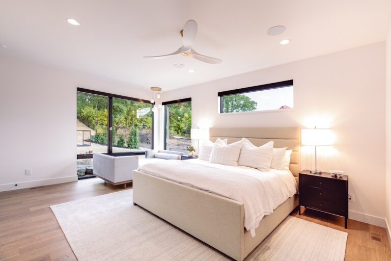 bedroom with large area rug under a queen bed and white oak hardwood floors white paint walls