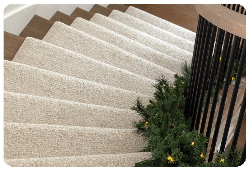view of a spiral staircase from above with wool carpet runner and holiday garland