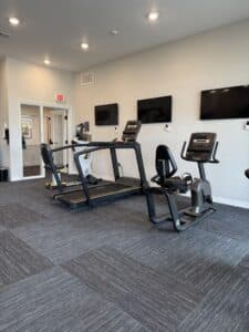 wellness room with treadmills white walls, tv screens, and grey large carpet tile flooring