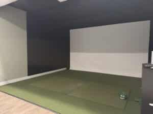 golf simulator room with large white screen green turf area in front of the screen and luxury vinyl plank flooring next to it
