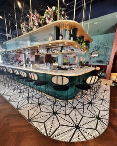 black and white mosaic tile in starburst pattern surrounding a bar with a wood floor installed in herringbone pattern