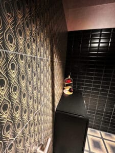 womens public bathroom with black and gold peacock tail pattern wall tile, black subway tile, and square pattern floor tile