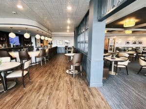 view of a bar and partial restaurant seating with luxury vinyl plank wood look floor in the bar and grey carpet tile in the restaurant
