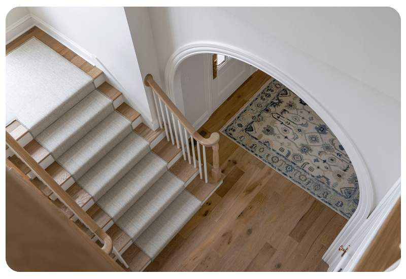Overhead view of a light oak hardwood hallway with a neutral stair runner and a blue patterned area rug
