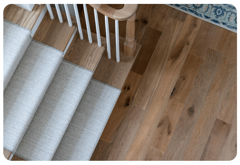 Wide-plank oak wood floor and blue stair runner in a Madison-area home; engineered hardwood is the top wood choice over radiant heat